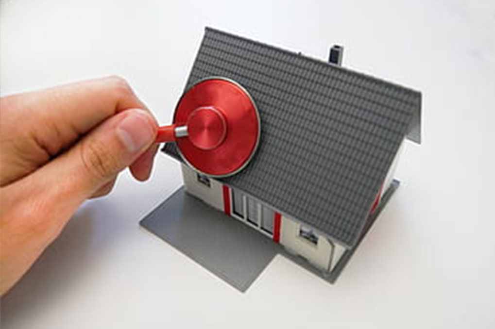 hand holding red stethoscope against toy house